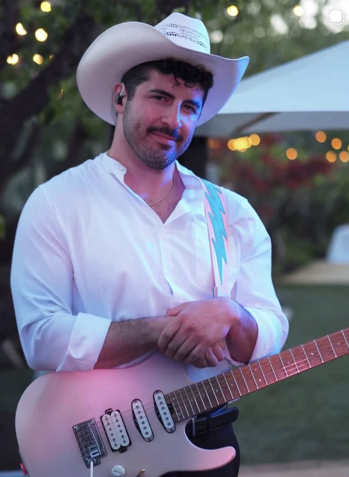 Andrew in a white cowboy hat with his guitar at an evening show